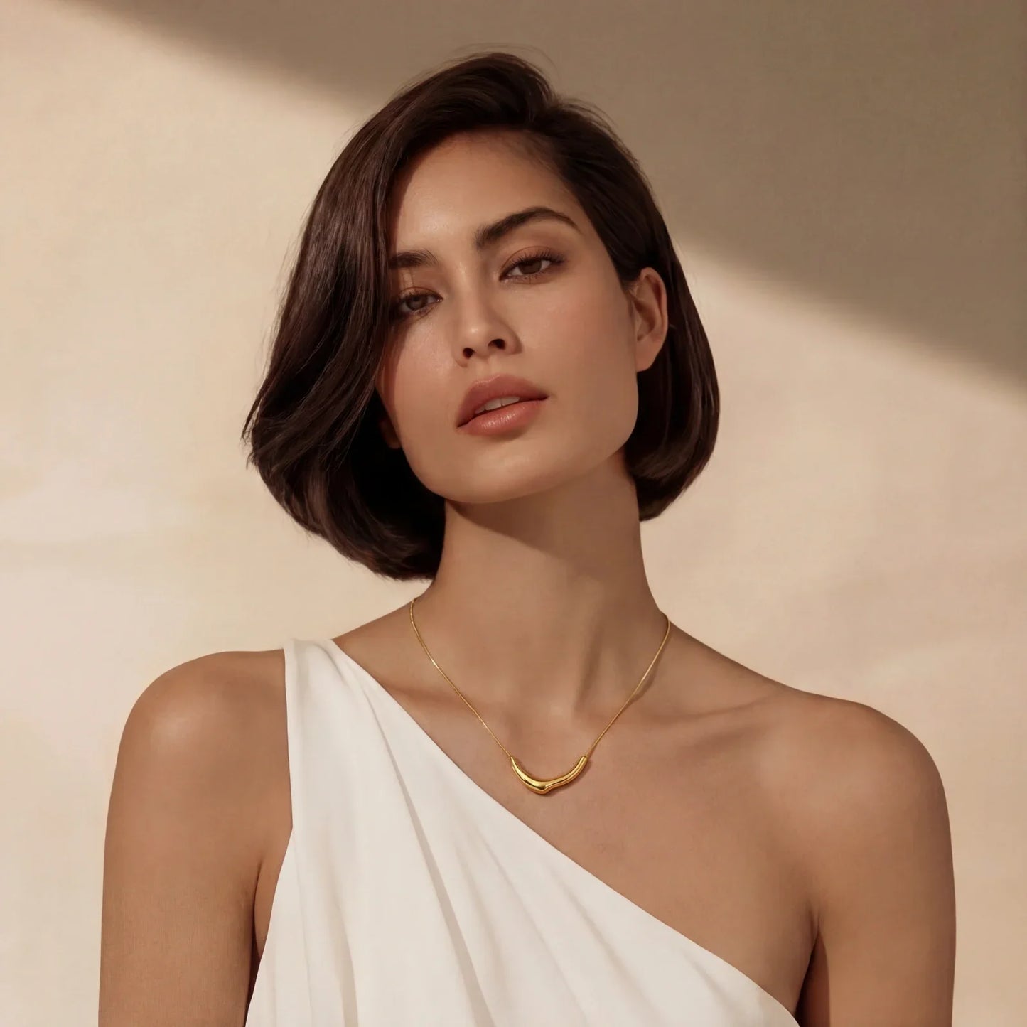 Woman wearing elegant gold crescent necklace with white one-shoulder top, minimalist home décor style