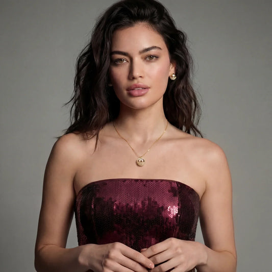 Elegant woman in burgundy sequin strapless top wearing gold pearl pendant necklace and matching earrings