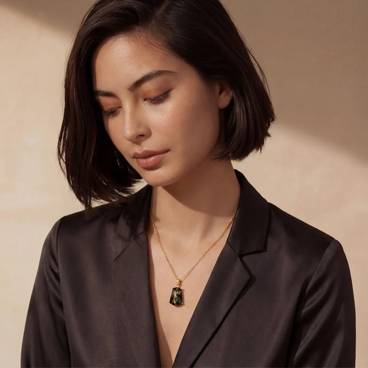 Woman wearing elegant gold necklace with green gemstone pendant, styled in chic black blazer
