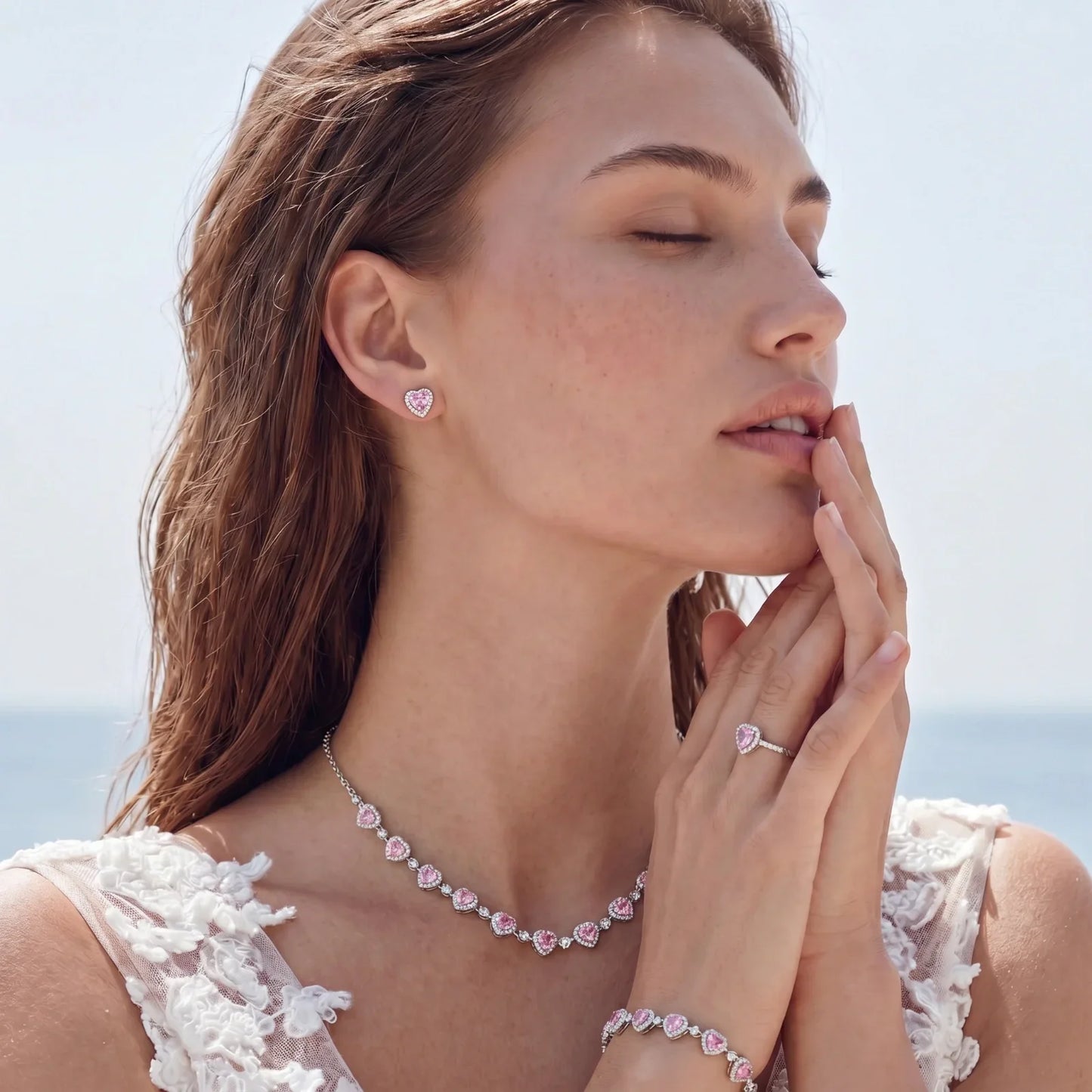 Woman wearing pink heart-shaped diamond necklace, earrings, ring, and bracelet by the ocean
