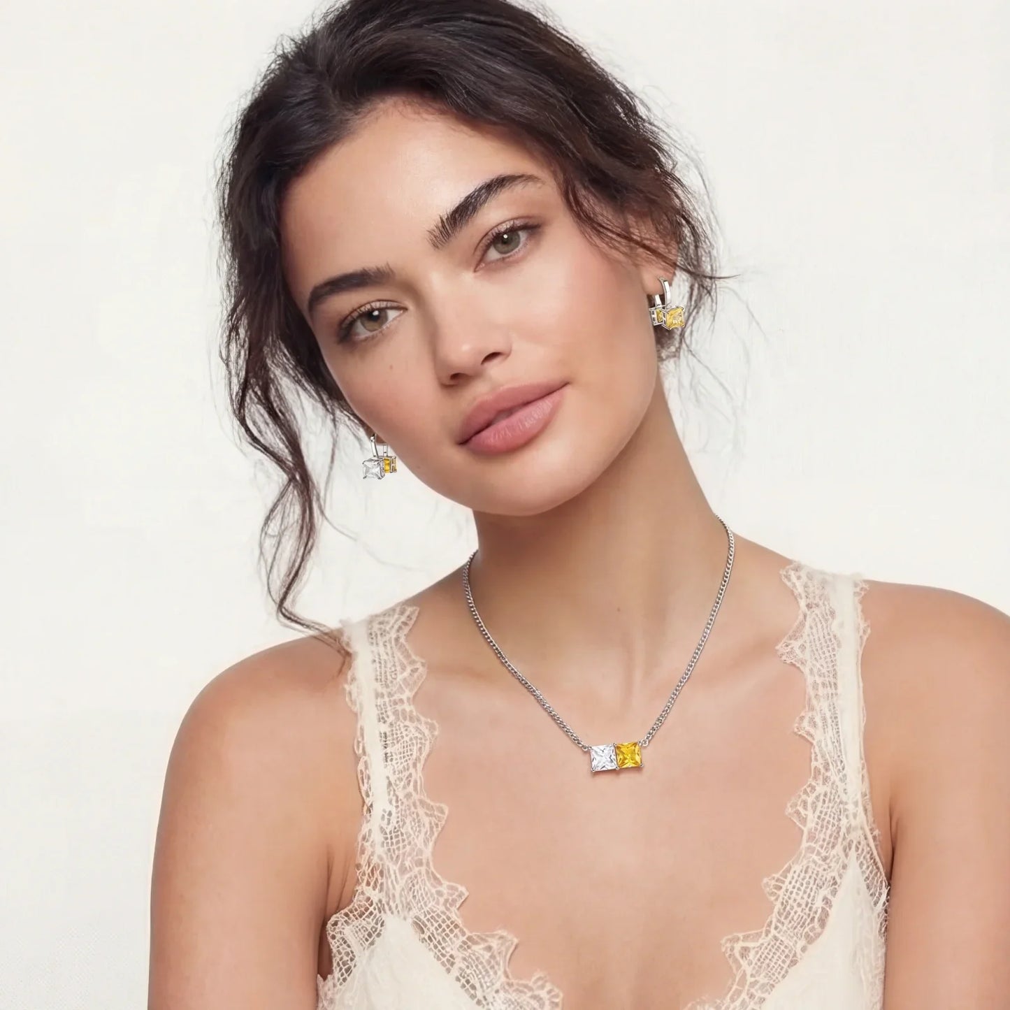 Elegant woman wearing silver necklace and earrings with yellow and clear square gems, lace top