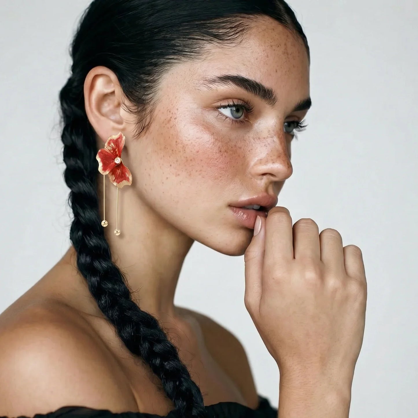 Red floral drop earrings with gold accents, worn by woman with braided hair