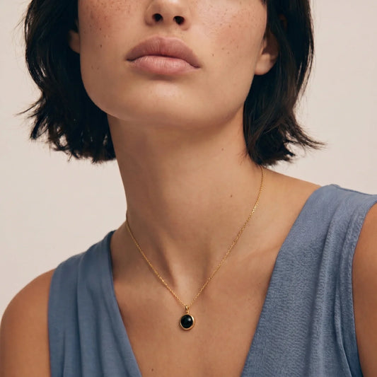 Gold chain necklace with black stone pendant, worn by woman in blue top