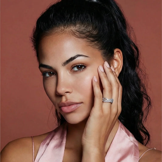 Elegant woman wearing a sparkling infinity ring, styled with soft pink silk top against warm backdrop