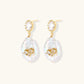 Gold-plated drop earrings with iridescent baroque pearls and crystal flower accents on cream background