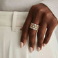 Elegant gold and silver statement ring with geometric pattern, worn on hand with neutral nails and white outfit.