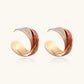 Sculptural gold-plated hoop earrings with diagonal purple and coral enamel stripes in twisted ribbon design
