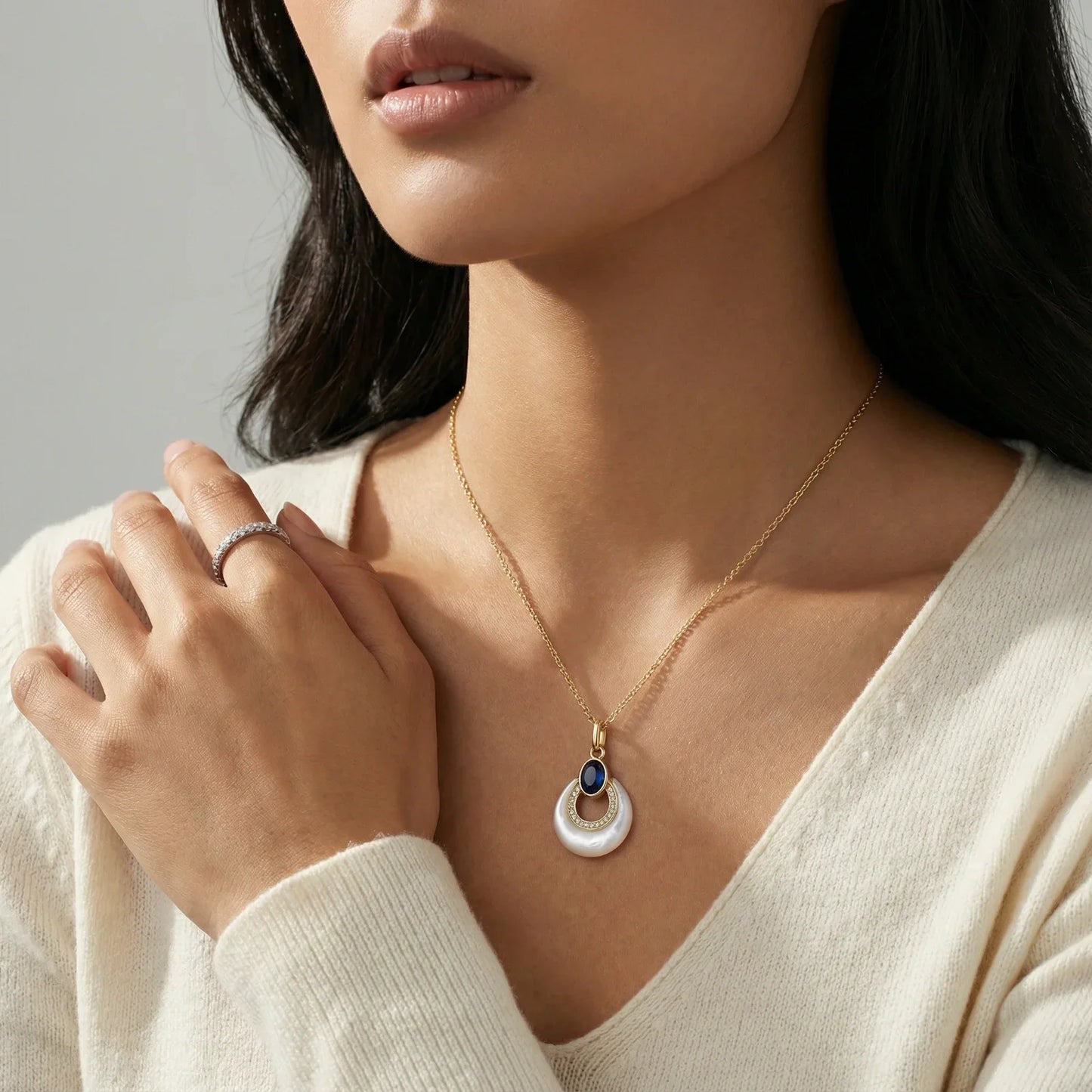 Elegant gold necklace with pearl and sapphire pendant, paired with diamond ring, styled for modern home décor