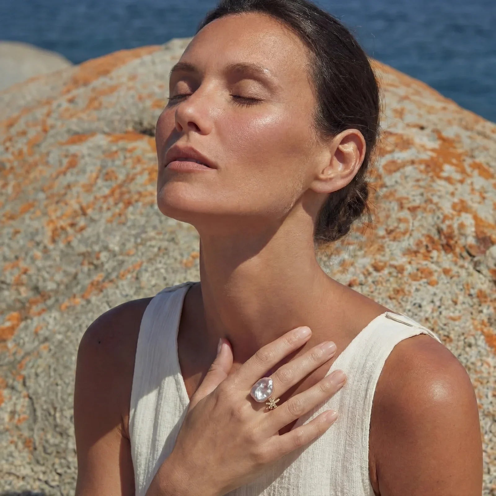 Woman wearing elegant pearl ring, enjoying coastal serenity with ocean and rocks background