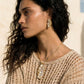 Elegant gold-tone necklace and matching earrings with pearl-like accents, styled with a textured knit top.