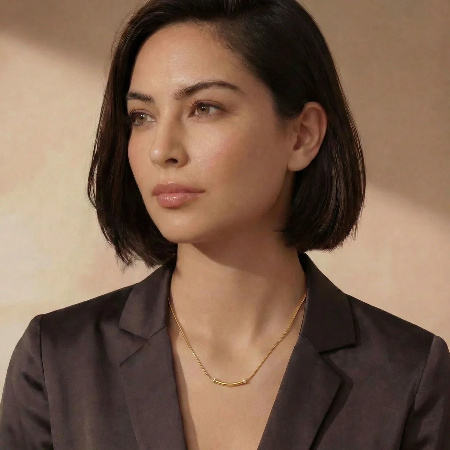 Woman wearing elegant gold bar necklace with diamonds, styled with dark blazer for modern sophistication.