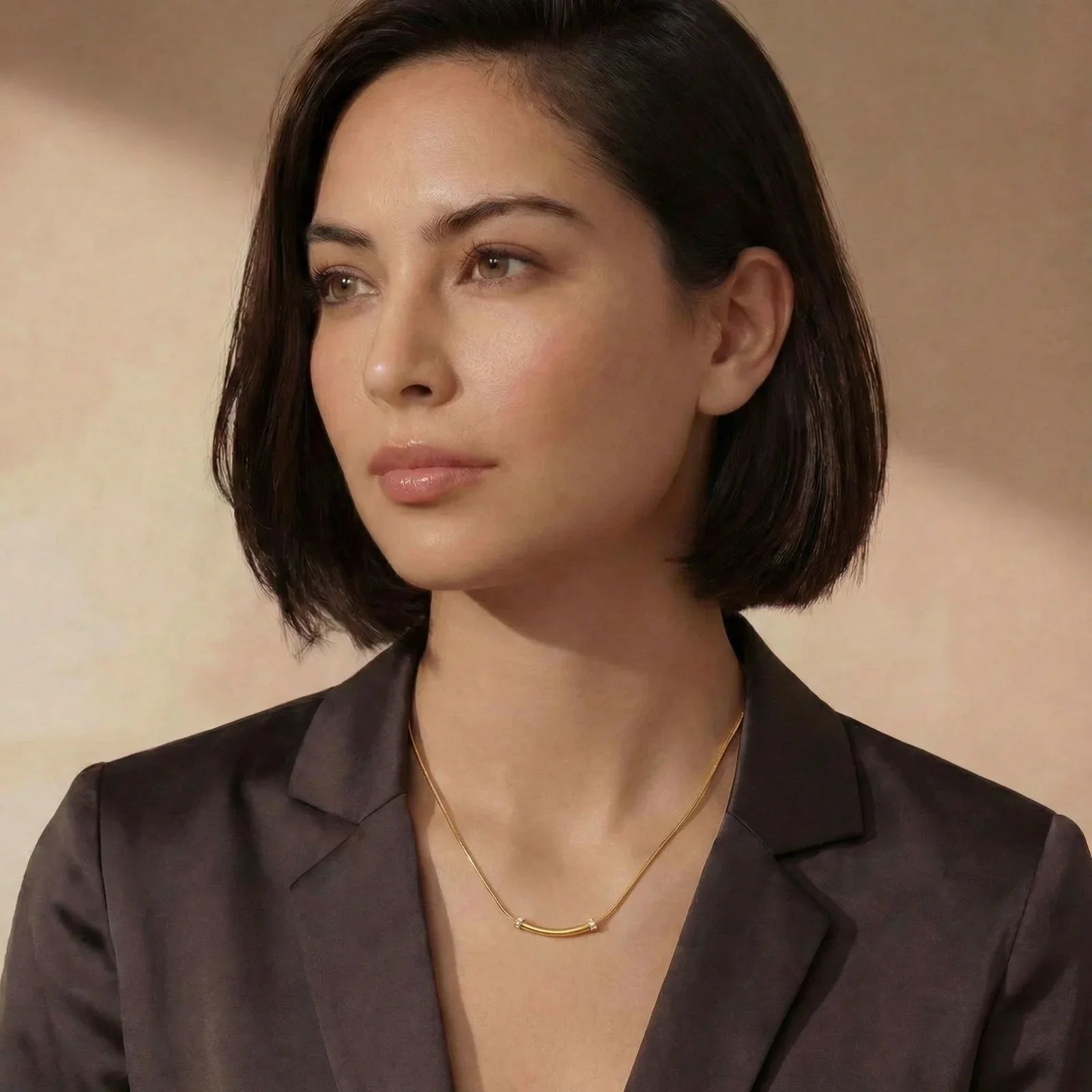 Woman wearing elegant gold bar necklace with diamonds, styled with dark blazer for modern sophistication.