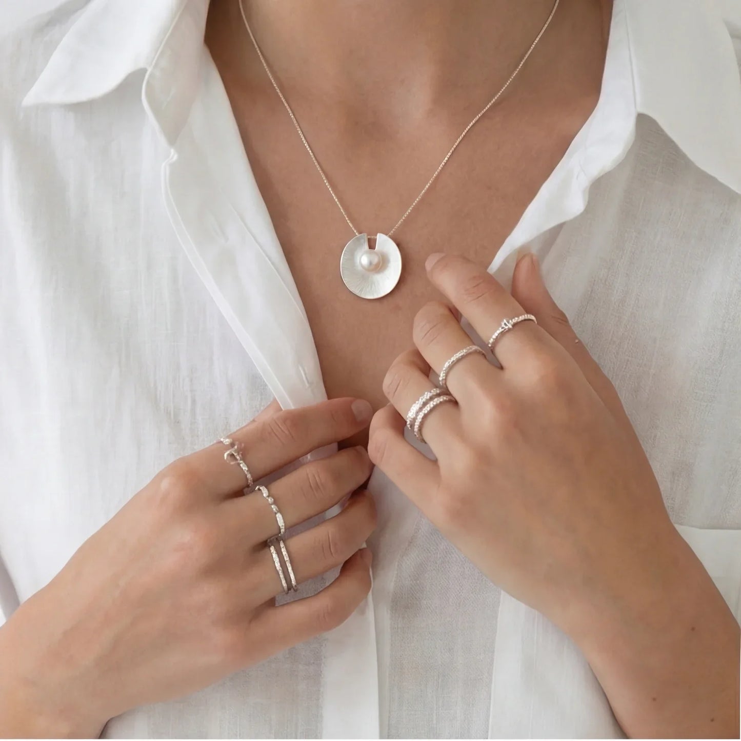 Elegant pearl pendant necklace and delicate stacking rings worn with a white blouse
