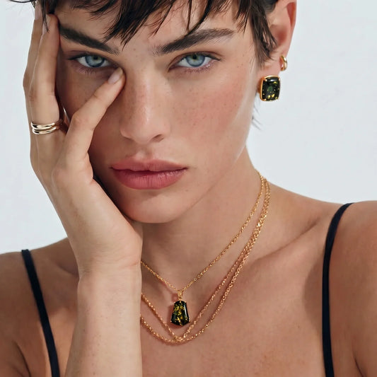 Woman wearing gold necklace with green gemstone pendant, matching earrings, and stacked rings