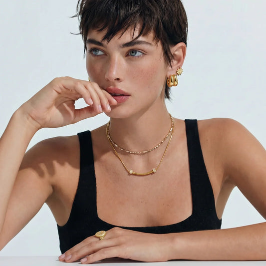 Woman wearing gold layered necklaces, hoop earrings, and a statement ring, styled for modern home décor
