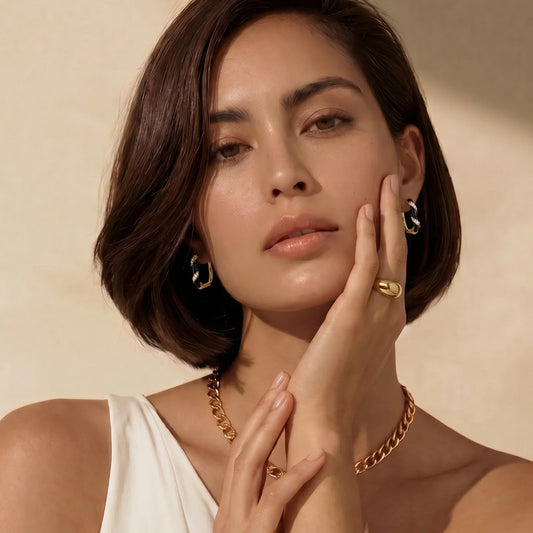 Woman wearing gold chain necklace, hoop earrings, and rings, styled for elegant home décor