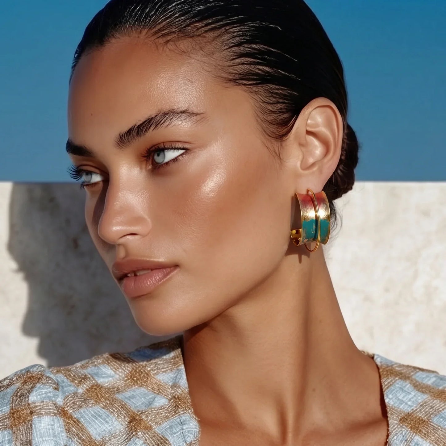 Woman wearing colorful gold hoop earrings, stylish checkered top against blue wall