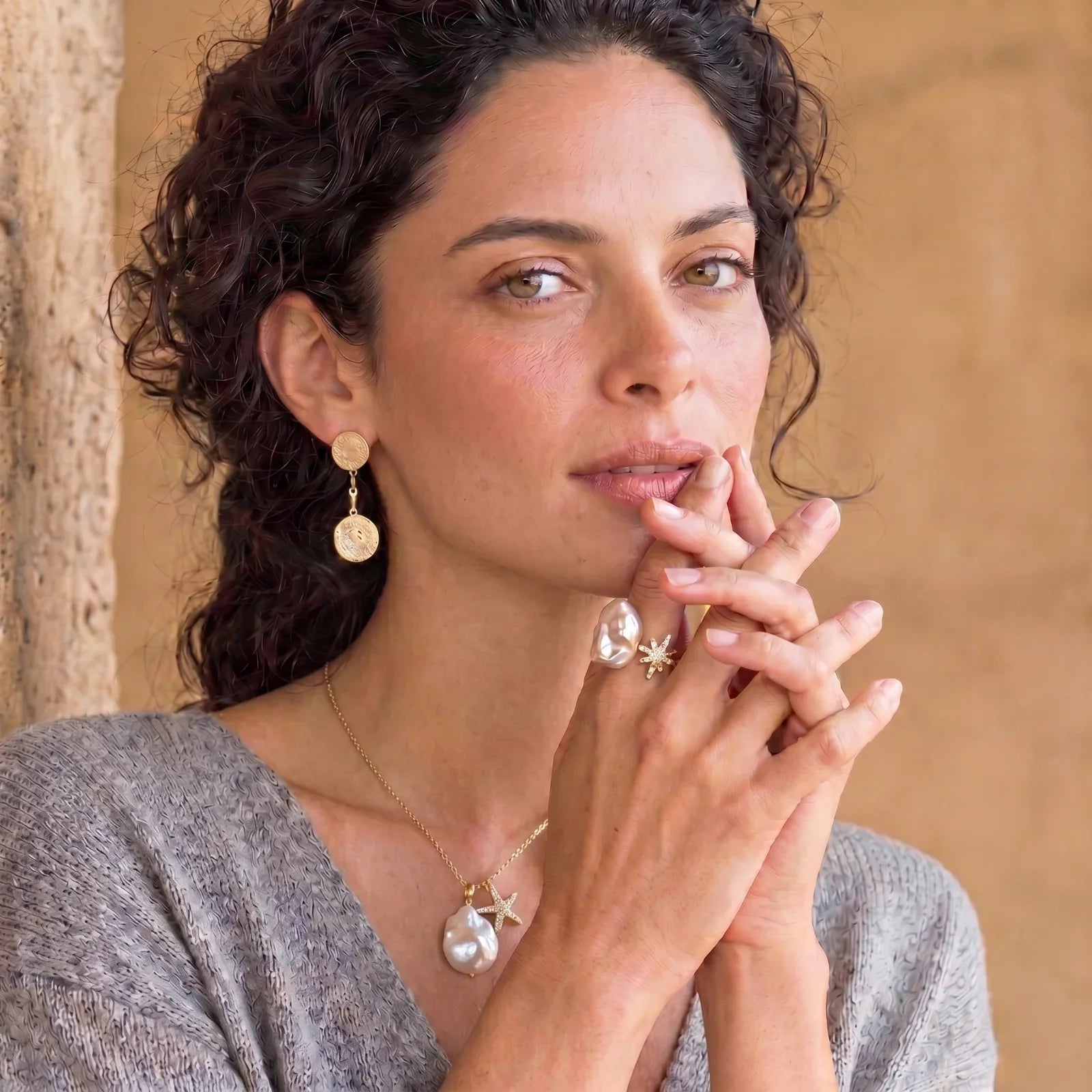 Woman wearing gold coin earrings, baroque pearl necklace, and starfish rings, styled for elegant home décor gifting.