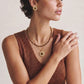 Woman wearing gold tiger eye pendant necklace and matching earrings, layered with beaded chain for boho style.