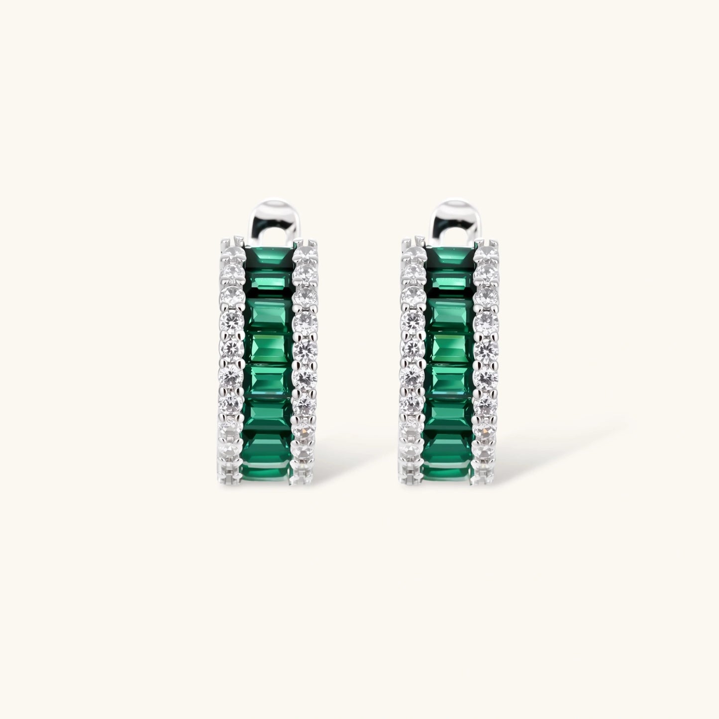 White gold plated jewelry set with emerald green rectangular stones and clear crystals in geometric rows on white background.