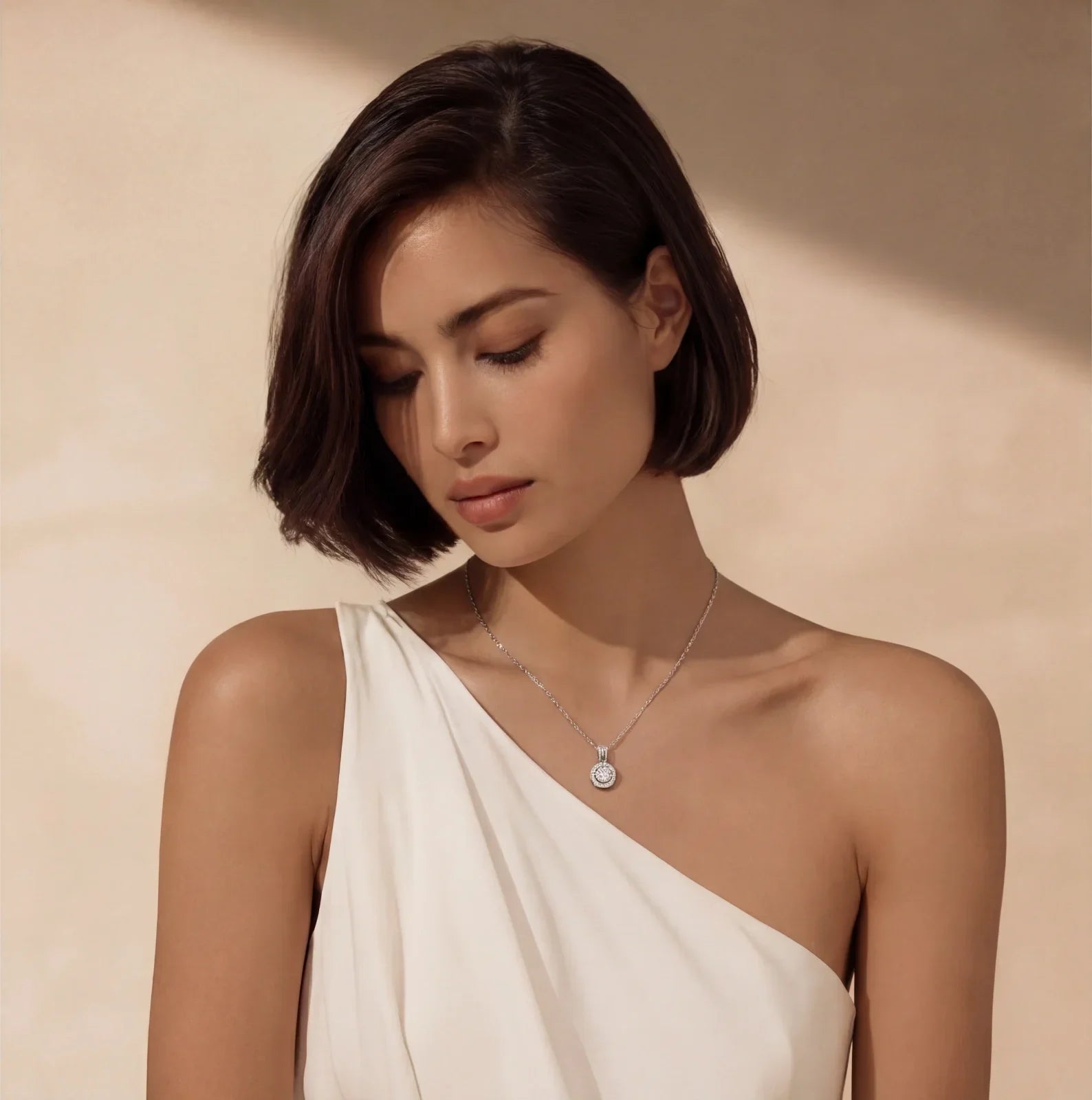 Elegant woman wearing a delicate diamond pendant necklace with a white one-shoulder dress.