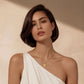 Woman wearing gold sunburst pendant necklace with rope chain, elegant white one-shoulder top
