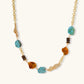 Statement necklace with gold chain, turquoise stones, amber beads, and wooden elements on cream background.