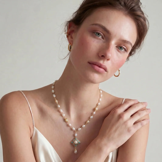 Elegant pearl necklace with gold accents and turquoise pendant, styled with gold hoop earrings.