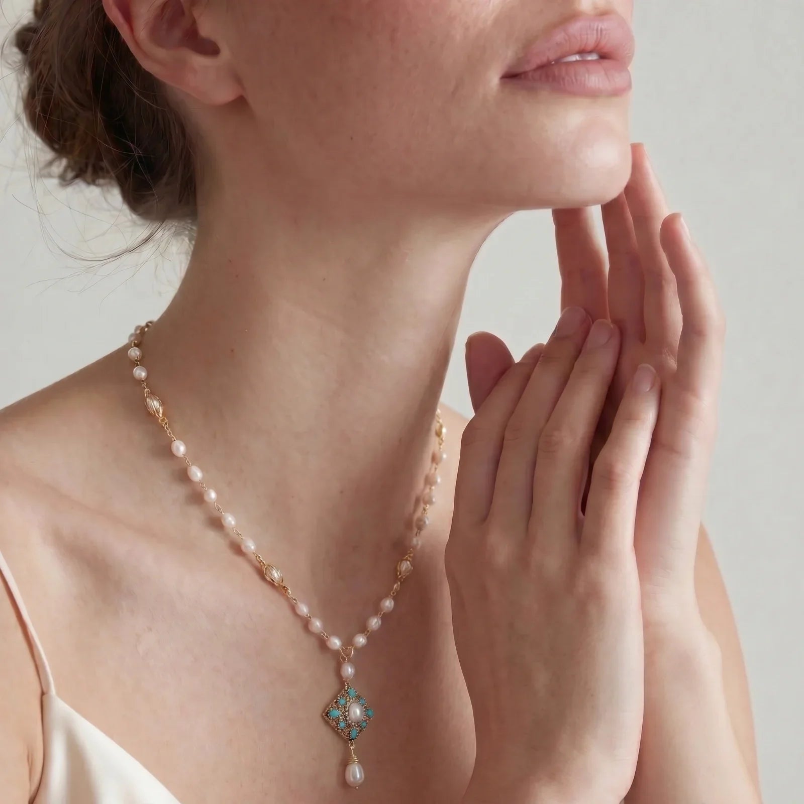 Elegant pearl necklace with turquoise pendant, gold chain, and delicate drop detail worn by woman