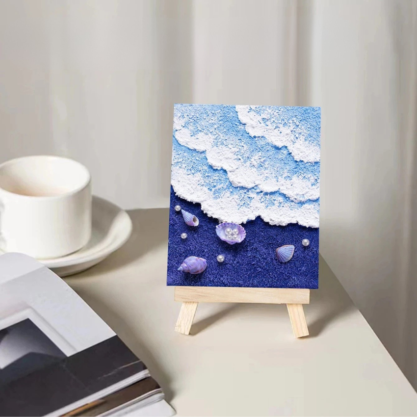 Mini easel with textured seascape art, blue and white clouds, seashells, and pearls decor.