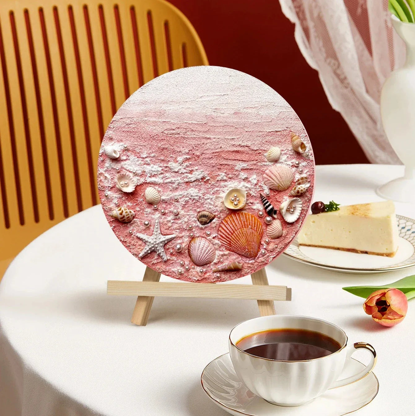 Handcrafted pink seashell art on easel, artisan home decor by Fansee Australia, on a table with coffee and cake.