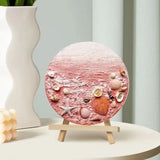 Round artisan home decor plaque with pink beach texture and seashells on small wooden easel