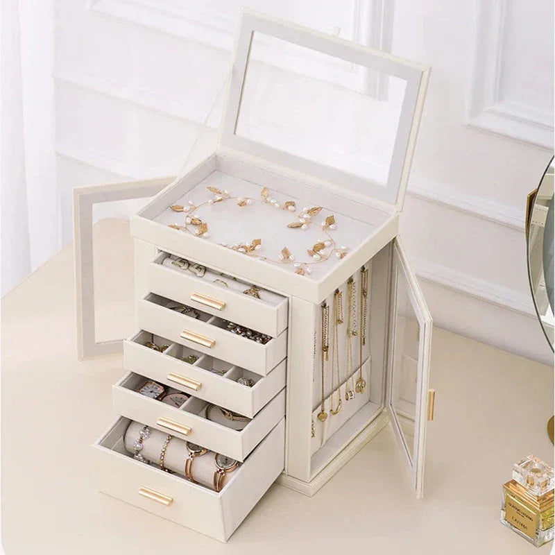 Elegant white jewelry box with gold handles, multiple drawers and compartments, displayed on a vanity table. 