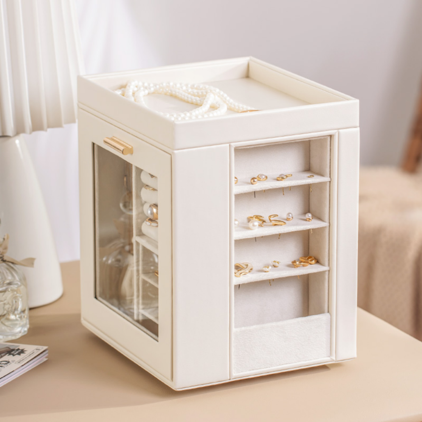 Elegant cream jewelry organizer box with glass panel and gold accents on a beige table