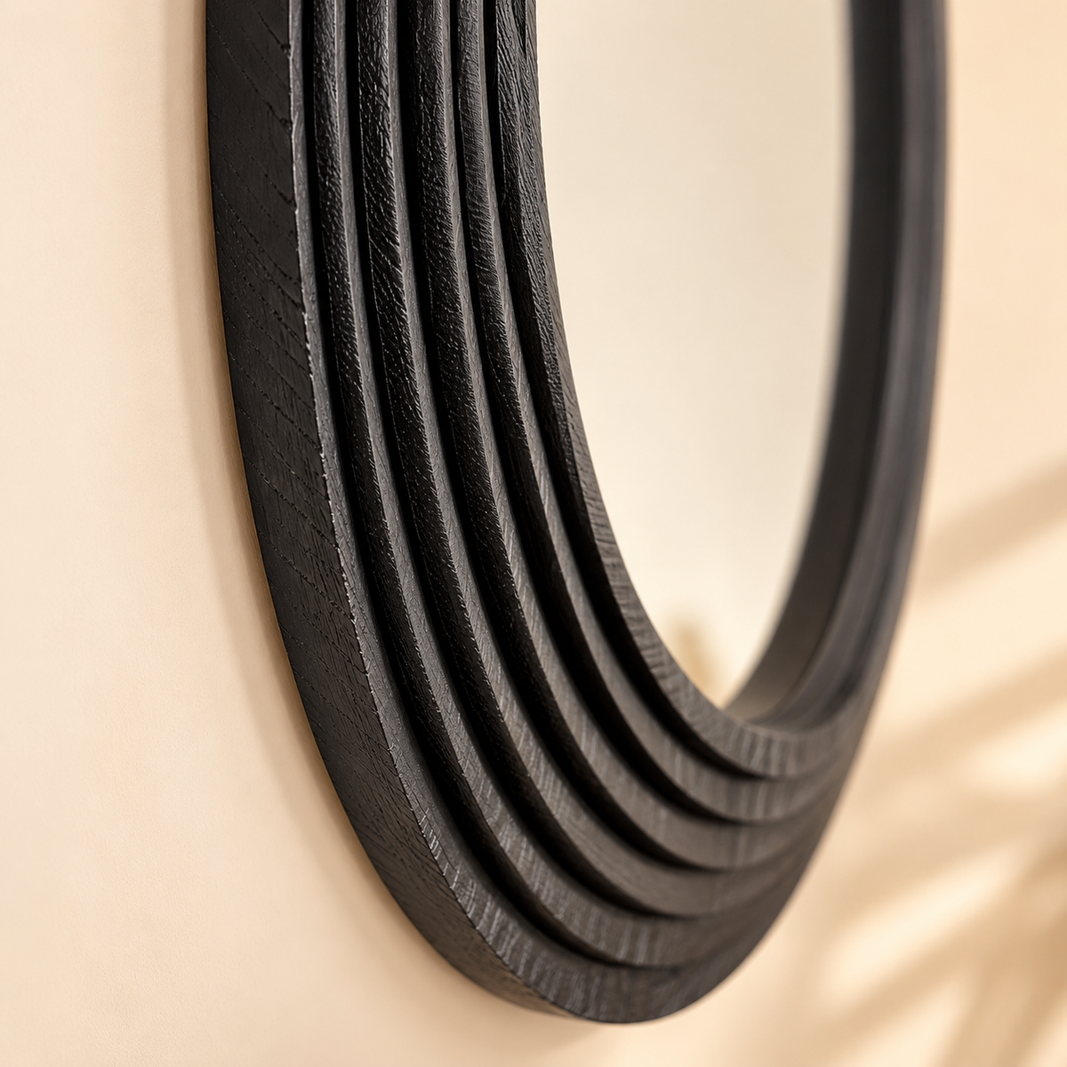A close-up of a round wall mirror with a thick, layered black frame mounted on a warm beige wall.